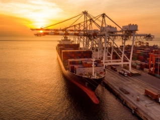 Crane loading cargo container at sunset